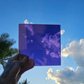 Purple chrome automotive window tint sample with a highly reflective mirror-like finish, held outdoors against a bright blue sky eflected across the surface. Purple chrome tint showcasing its vibrant colour, reflective appearance, and distinctive custom vehicle styling potential.
