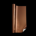 Roll of metallic copper automotive styling film partially unrolled to reveal its glossy reflective surface and peeled-back backing corner, displayed against a solid black background. Copper vinyl wrap featuring a bold metallic finish for custom vehicle styling.