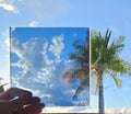 Steel blue chrome automotive window tint sample held against a palm tree and blue sky with clouds, showcasing a highly reflective mirror-like finish. Steel blue chrome tint highlighting its warm metallic colour and distinctive reflective appearance for custom vehicle styling.
