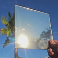 Hyper chrome automotive window tint sample with a highly reflective mirror-like finish, held outdoors against a bright blue sky with palm trees reflected across the surface. Hyper chrome tint showcasing its vibrant colour, reflective appearance, and distinctive custom vehicle styling potential.

